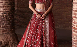 Bazaar light burgundy velvet Pakistani lehenga choli by Waqas Shah, front view with organza dupatta between brick pillars