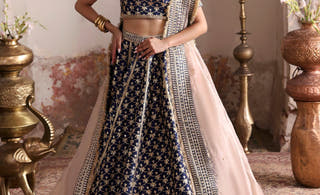 Geet navy blue raw silk lehenga choli by Waqas Shah, front view with champagne tissue dupatta under a white carved arch