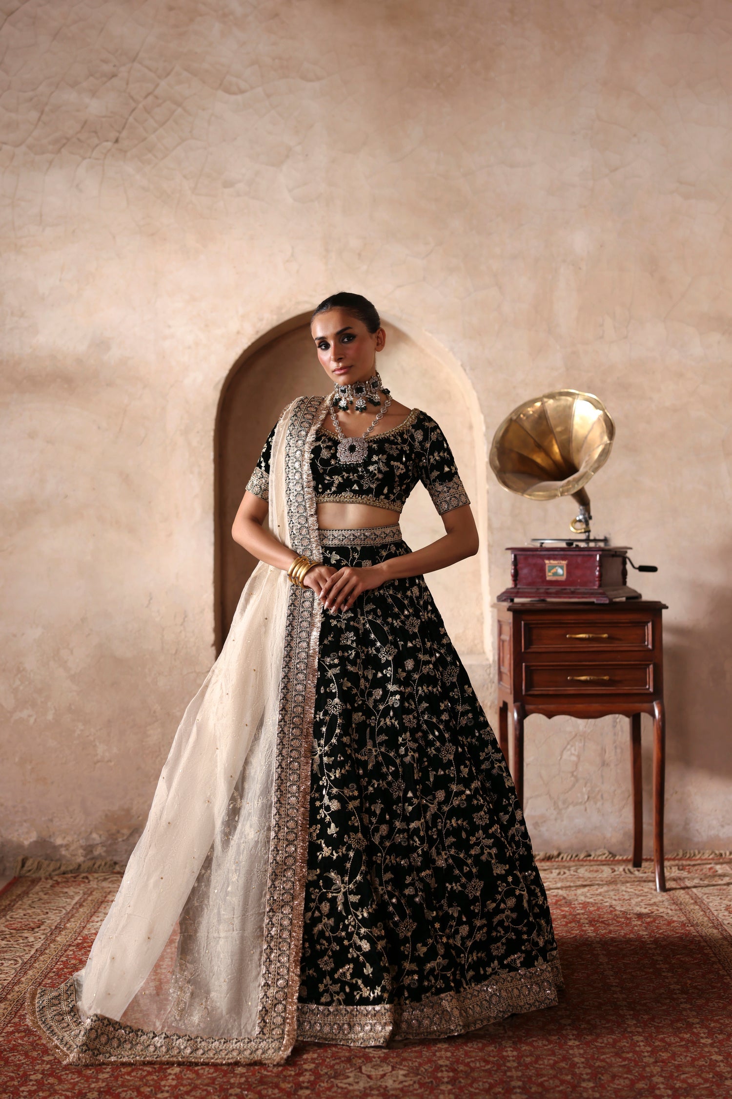 Taseer dark green velvet lehenga choli by Waqas Shah with an ivory tissue dupatta, full front view by a haveli arch