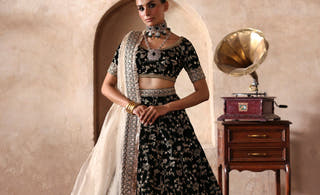 Taseer dark green velvet lehenga choli by Waqas Shah with an ivory tissue dupatta, full front view by a haveli arch