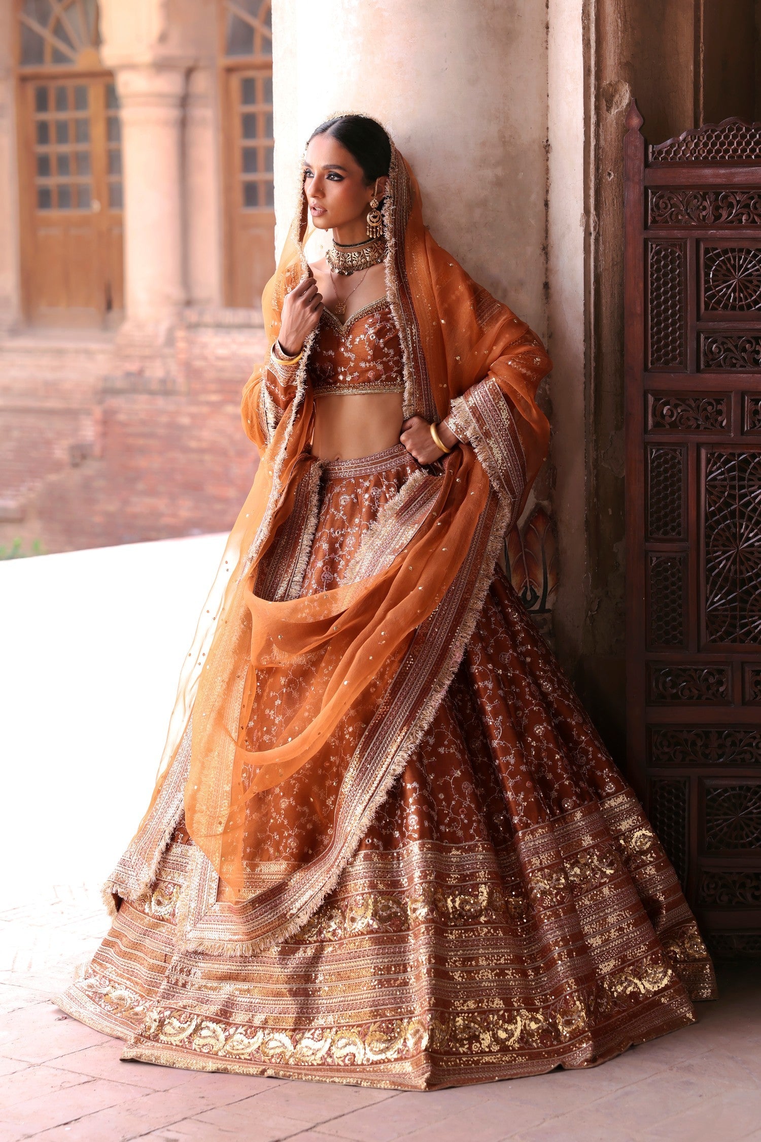 Gurleen rust brown bridal lehenga choli with organza dupatta under haveli arches, by Waqas Shah